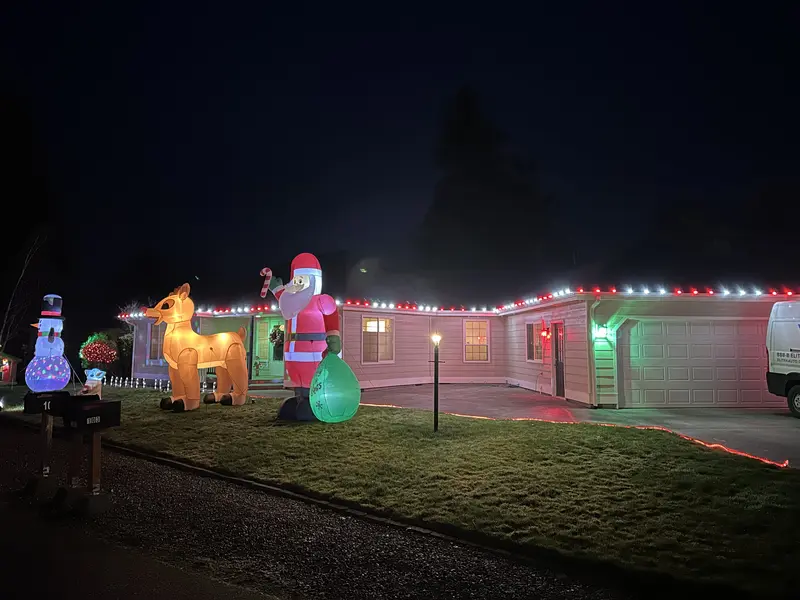 A home lit with candy-cane striped roofline lights and holiday inflatables
